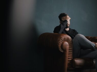 a man holds his head while sitting on a sofa