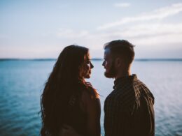 man and woman standing while looking each other near body of water