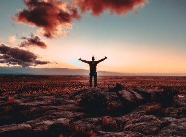 person standing on rock raising both hands