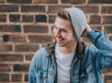 man holding the back of his head while smiling near brick wall