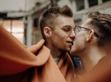 man in black framed eyeglasses kissing woman in red dress